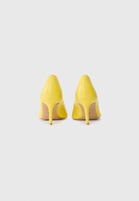 Scarpe gialle con tacco alto, punta affusolata e finitura in pelle liscia. Presentano un tacco sottile e un discreto dettaglio del logo interno.