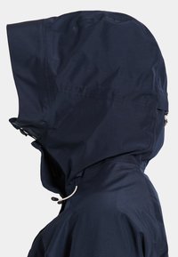 Tmavomodrá nepremokavá bunda s kapucňou a nastaviteľným sťahovaním, bočný profil ukazuje hlavu a hornú časť ramien.