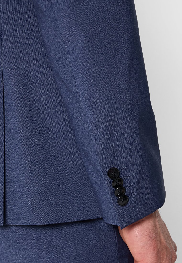 Giacca da abito blu navy in primo piano, con tessuto testurizzato, vestibilità strutturata e quattro bottoni neri sui polsini per dettagli di chiusura.