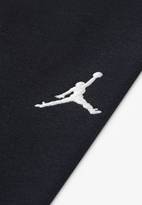 Black textile featuring a white embroidered Jumpman logo. The fabric has a smooth texture and a slightly stretchy appearance.
