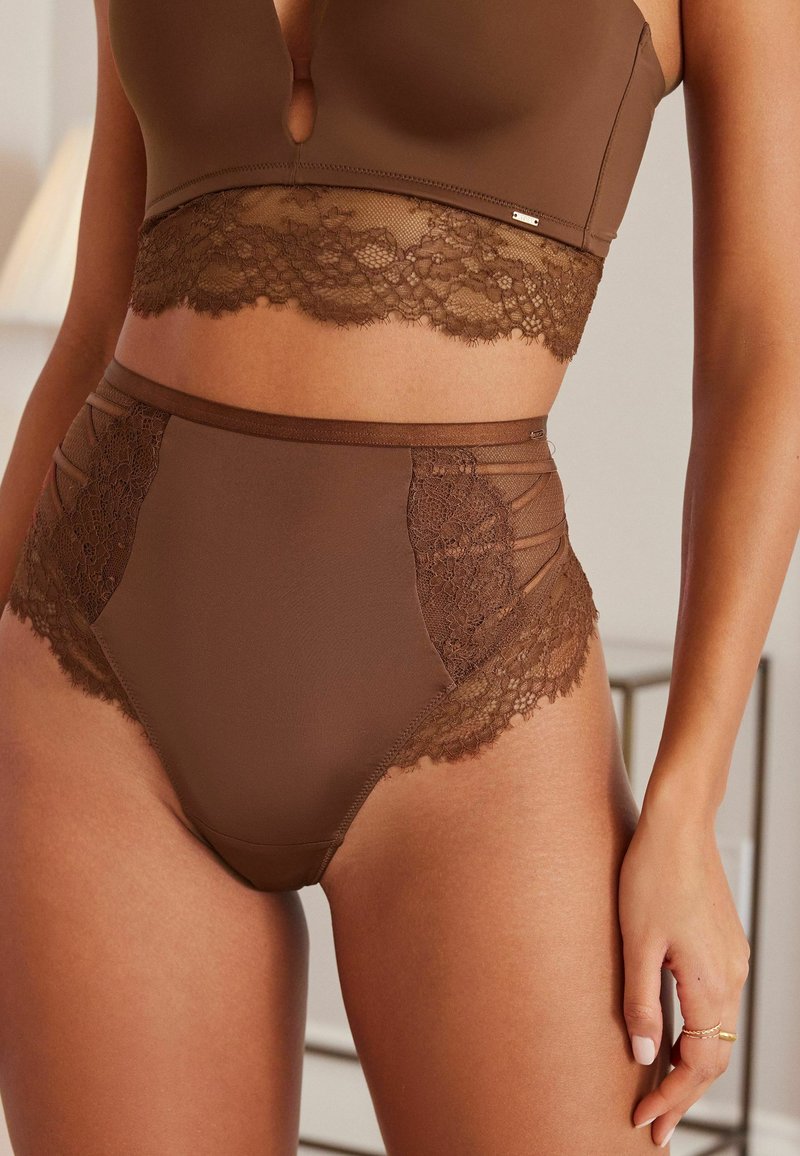 Braunes Dessous-Set bestehend aus einem Bralette mit Spitze und einem hochgeschnittenen Höschen mit Spitzen-Einsätzen, das glatte Texturen und nahtlose Kanten betont.
