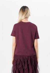 Woman with long blonde hair facing away, wearing a plain burgundy short-sleeve top and tiered ruffled burgundy skirt.