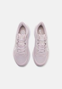 Běžecké boty Nike v světle růžové síťovině, s bílými akcenty, kulatými tkaničkami a polstrovanou podrážkou. Design je štíhlý a moderní.