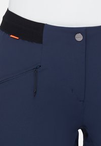 Marineblauwe sportbroek met een zwarte tailleband, voorzien van een zichtbare ritszak, trekkoord en reflecterende details. Duurzame stof.