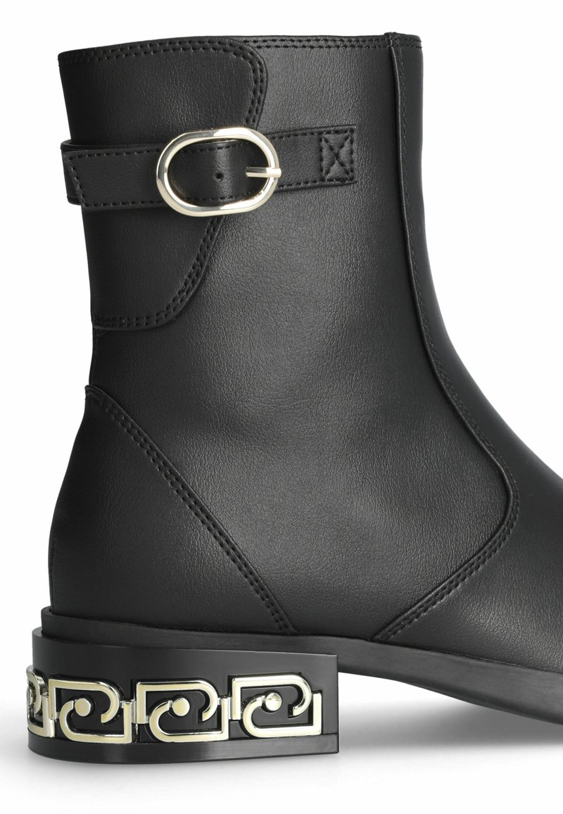 Stivale alla caviglia in pelle nera con una fascia decorativa a fibbia e un distintivo tacco metallico a motivo. Texture liscia e design elegante.