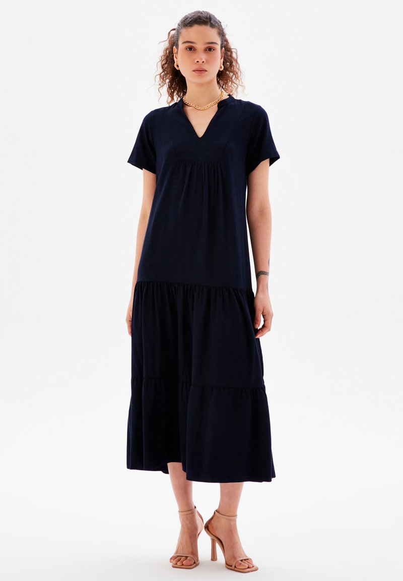 Vestido midi de color azul marino con volantes, mangas cortas, escote en V y textura de tela suave. Acentuado con un sutil fruncido en el busto.