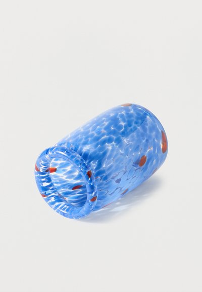 Gobelet en verre bleu avec des taches rouges, couché sur le côté sur un fond blanc.