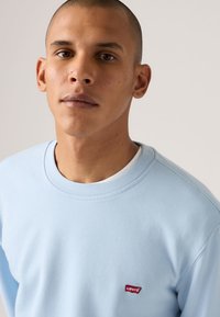 Ανοιχτό μπλε φούτερ από μαλακό ύφασμα, με στρογγυλή λαιμόκοψη και μικρό κόκκινο λογότυπο Levi's στο αριστερό στήθος. Λείο ύφασμα, άνετη εφαρμογή.