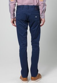 Tmavě modré chinos kalhoty s úzkým střihem, vyrobené z bavlny. Mají zadní kapsy a poutka na pásek, doplněné hnědými botami.