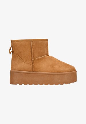 Sandfarbene Wildleder-Ankle-Boots mit dicker Plateausohle, runder Spitze und Schlaufe an der Rückseite. Sichtbare angenähte Nähte an den Seiten.