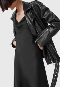 Zwarte leren motorjack met zilveren ritsen en drukknoopsluitingen, gelaagd over een zwart satijnen slipdress met een kraaghals.