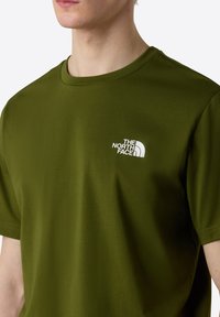 Olive vihreä lyhythihainen t-paita, joka on valmistettu sileästä kankaasta ja jossa on valkoinen "THE NORTH FACE" -logo vasemmassa rinnassa.