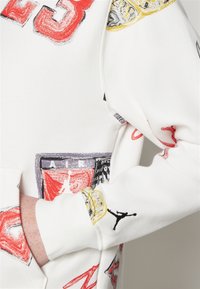 Sudadera blanca con gráficos vibrantes y estampados, que incluyen números rojos, logotipos e ilustraciones en negro y amarillo. Textura suave.
