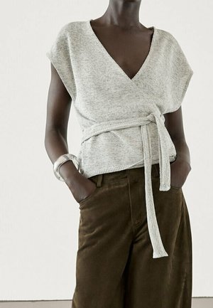 Light gray wrap top with a V-neck, short sleeves, and a tie at the waist. Paired with dark brown wide-leg pants. Smooth knit texture.