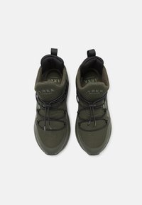 Zapatillas de malla verdes con un cuerpo texturizado, cordones negros, puntera reforzada y una lengüeta en el collar para facilitar su uso.