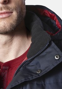 Dunkelblaue Jacke mit einem fleecegefütterten Kragen und rotem Innenfutter. Verfügt über silberne Druckknöpfe und ein strukturiertes Material im Halsbereich.