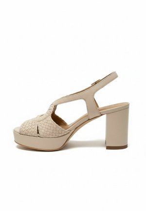 Beige hoge hak sandaal met geweven voorriem, open teen, slingback enkelriem en blokhak op een witte achtergrond.