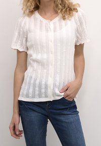 Vit knappen-up blus med korta ärmar, med vertikala vävda mönster och en strukturerad yta. Kombinerad med denimjeans.