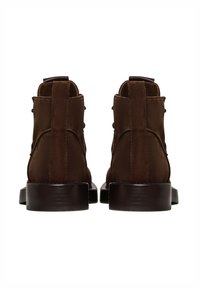 Paire de bottines en daim brun foncé vues de dos, avec languettes de tirage et talons bas épais sur un fond blanc.