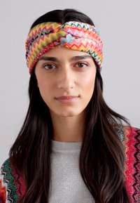 Bunte, gewebte Haarband mit einem gedrehten Design und Zickzackmustern in Pink, Blau und Gelbtönen auf einer glatten Oberfläche.