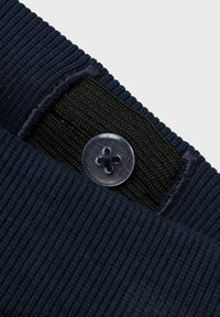 Tejido de canalé azul marino con una banda elástica negra, que presenta un botón de plástico transparente con un diseño de cruz, destacando la textura y las capas.
