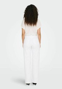 Pantalones blancos de pierna ancha con dos bolsillos traseros, combinados con una blusa de corte holgado de color beige claro. Textura suave, diseño casual.