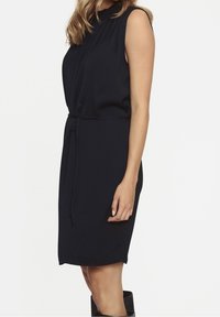 Marinblå ärmlös klänning med hög halsringning, intryckt midja och rak skärning. Tillverkad av mjukt, slätt tyg med en knytbälte detalj.