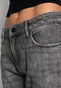 Šedé džíny z denimu s detailním záběrem na pas, zapínání na knoflík a přední kapsu s jemnou opotřebovanou texturou.