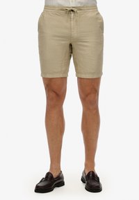 Pantalones cortos de lino beige con waistband elástico y cordón, con bolsillos laterales y un ajuste holgado, de longitud por encima de la rodilla.
