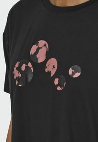 Camiseta negra de manga corta con un patrón abstracto circular en rosa y negro en el frente. Tejido suave con un ajuste relajado.