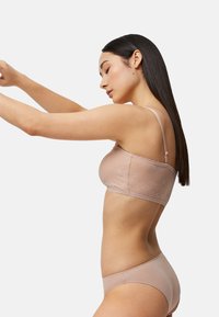 Bralette de encaje en beige claro con tirantes finos y borde festoneado, combinado con bragas hipster lisas a juego. Patrón sutilmente texturizado.