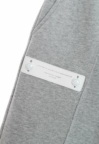 Pantalones de chándal de algodón grises con una textura suave, que presentan una etiqueta blanca cosida en el costado y dos botones a presión visibles.