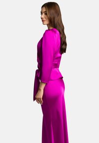 Magenta satynowa sukienka z dopasowaną górą, długimi rękawami i wiązanym w talii paskiem. Spódnica przechodzi w długi krój, eksponując gładką teksturę.