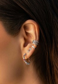 Hopeat korvakorut, joissa on monimutkaisia muotoiluja: värikäs rengas jalokivillä, kerroksittain pinottuja bändejä kirkkailla kivillä ja pieni nuoli-stud.