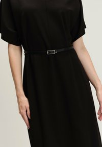 Černé šaty z měkké tkaniny, s volným střihem, krátkými rukávy, staženým pasem s úzkým černým pásem a minimalistickými designovými detaily.