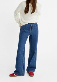 High waist wijde jeans in medium blauwe denim, met een klassiek ontwerp van vijf zakken en contrasterende stiksels, gecombineerd met een crème kleurige gebreide trui.