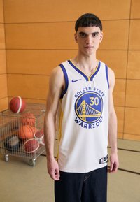 Bílá basketbalová dres s modrými a žlutými akcenty, s nápisem a logem "GOLDEN STATE WARRIORS". Síťovina, bezrukávový design.