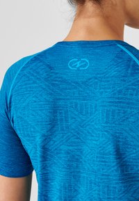 Camisa deportiva azul con un patrón texturizado, que presenta mangas raglán y un cuello redondo. Logo mostrado en la parte posterior.