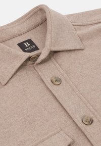 Bežová vlněná košile s límečkem, dvěma knoflíky a kapsičkou. Na látkovém štítku je značka "BOGGI MILANO".