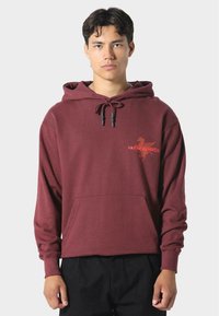Felpa bordeaux con tasca a marsupio, coulisse regolabile e grafica arancione a contrasto. Realizzata in tessuto morbido e strutturato.