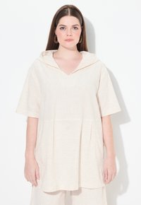 Túnica a rayas color crema con escote en V y capucha, mangas cortas y un corte relajado, que presenta una tela texturizada y un dobladillo redondeado.