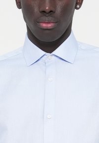 Φωτεινό μπλε πουκάμισο με κουμπιά, με υφή, που διαθέτει μυτερό γιακά και λευκά κουμπιά. Απλός σχεδιασμός, χωρίς ορατά σχέδια ή διακοσμητικά στοιχεία.