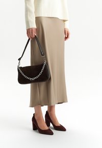 Brązowa torebka z zamszu z srebrnym łańcuchem. Połączona z beżową satynową spódnicą i brązowymi zamszowymi szpilkami na słupku.