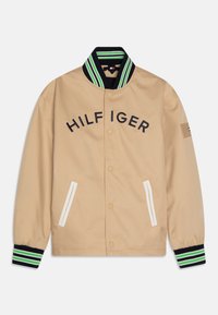 Beige bomber jacket with black and green striped collar, embroidered "HILFIGER" lettering, white pocket accents, and elasticated cuffs.