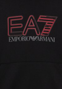 Črna kapa s potiskom velike EA7 blagovne znamke v rdeči in beli barvi. Mehka tkanina z rahlo teksturo in izrazitimi detajli šivov.