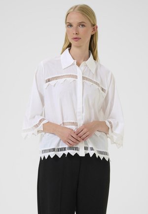 Weißes Shirt mit kurzen Ärmeln, das durch ausgeschnittene Zickzackdetails am Oberteil und Saum besticht. Druckknopf-Design aus leichtem Stoff.