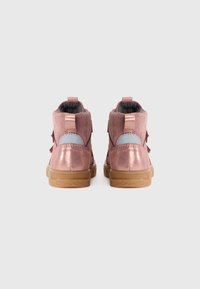 Ein Paar pinkfarbene Kleinkinderstiefel mit reflektierenden Einsätzen, Obermaterial aus Wildleder und Gummisohlen, von hinten auf einem schlichten Hintergrund gesehen.