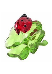 Coccinella di cristallo sopra un trifoglio verde. La coccinella è rossa con accenti neri, mentre il trifoglio presenta una superficie verde liscia e sfaccettata.