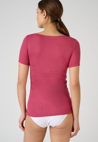 Haut à manches courtes de couleur brique, fabriqué en tissu léger avec une coupe ajustée et un grand col. Aucun motif ni accent visible.