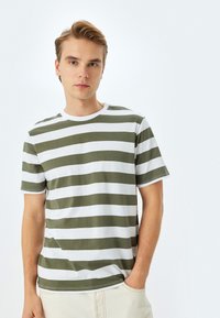Grøn- og hvidstribet T-shirt i bomuldsmateriale, rund hals, korte ærmer. Har vandrette striber i lige bredde.